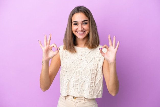 Jovem mulher caucasiana isolada em fundo roxo mostrando sinal de ok com as duas mãos