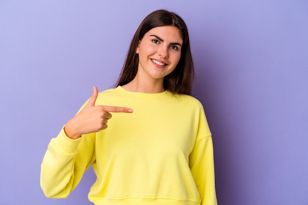 Jovem mulher caucasiana isolada em fundo roxo pessoa apontando com a mão para um espaço de cópia de camisa, orgulhosa e confiante