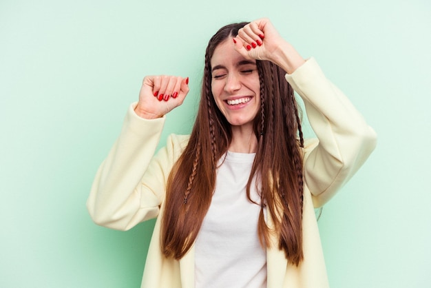 Jovem mulher caucasiana isolada em fundo verde comemorando um dia especial pula e levanta os braços com energia