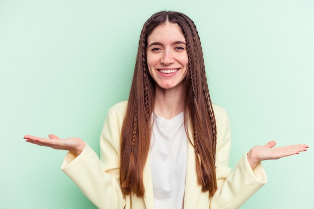 Jovem mulher caucasiana isolada em fundo verde faz escala com braços se sente feliz e confiante