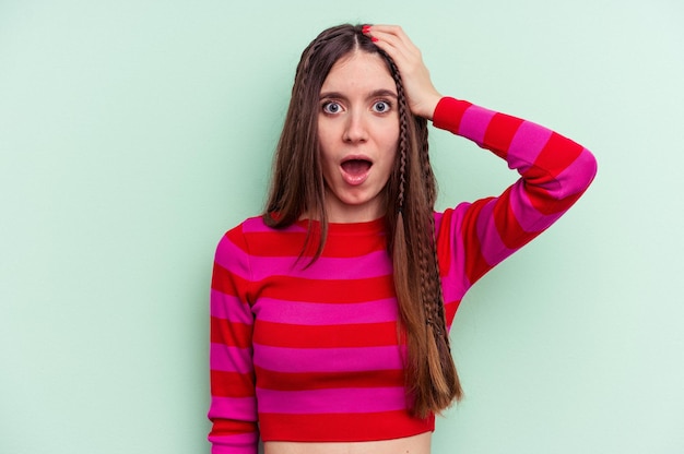 Jovem mulher caucasiana isolada em fundo verde sendo chocada, ela se lembrou de uma reunião importante.