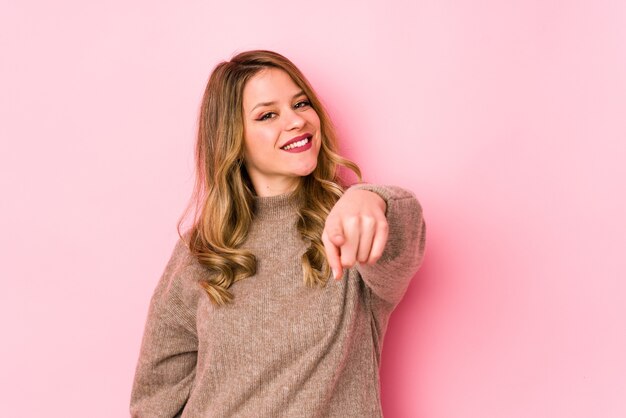 Jovem mulher caucasiana isolada em sorrisos alegres de parede rosa, apontando para a frente.