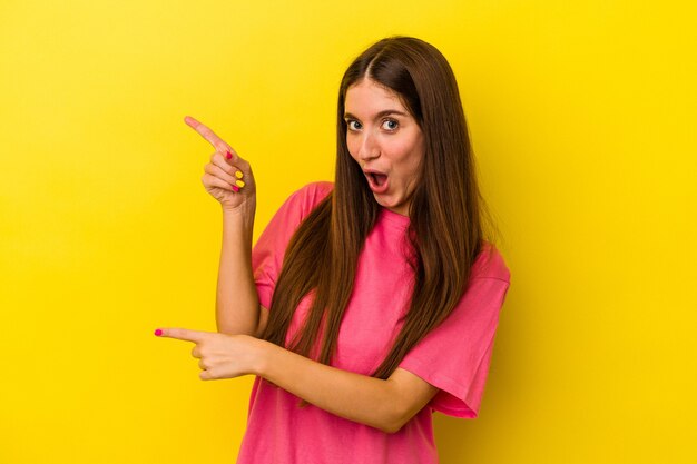 Jovem mulher caucasiana isolada em um fundo amarelo, apontando com os indicadores para um espaço de cópia, expressando entusiasmo e desejo.