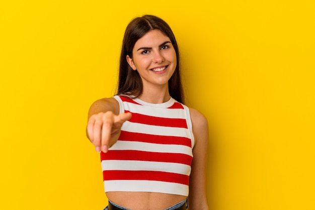 Jovem mulher caucasiana isolada em um fundo amarelo, apontando para a frente com os dedos.