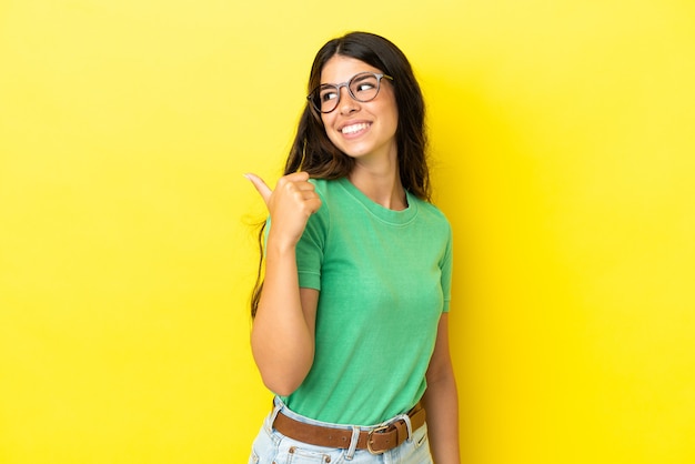 Jovem mulher caucasiana isolada em um fundo amarelo apontando para o lado para apresentar um produto