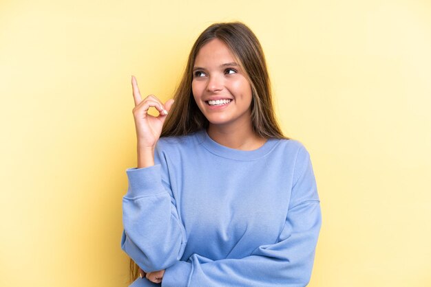 Jovem mulher caucasiana isolada em um fundo amarelo apontando para uma ótima ideia