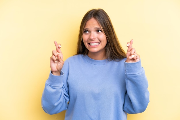 Jovem mulher caucasiana isolada em um fundo amarelo com os dedos se cruzando e desejando o melhor