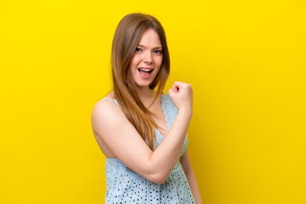 Jovem mulher caucasiana isolada em um fundo amarelo comemorando uma vitória