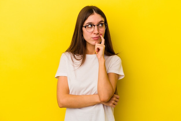 Jovem mulher caucasiana, isolada em um fundo amarelo, contemplando, planejando uma estratégia, pensando na forma de um negócio.