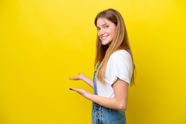 Jovem mulher caucasiana isolada em um fundo amarelo, estendendo as mãos para o lado para convidar para vir