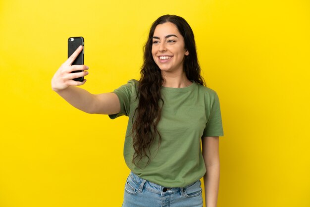 Jovem mulher caucasiana isolada em um fundo amarelo fazendo uma selfie