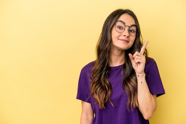 Jovem mulher caucasiana isolada em um fundo amarelo, mostrando o número um com o dedo.