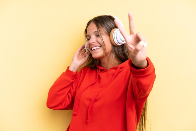 Jovem mulher caucasiana isolada em um fundo amarelo ouvindo música e cantando