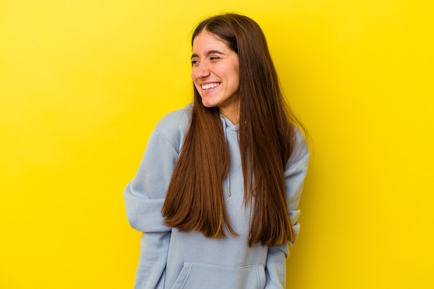 Jovem mulher caucasiana, isolada em um fundo amarelo, ri e fecha os olhos, sente-se relaxada e feliz.