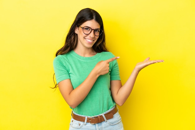 Jovem mulher caucasiana isolada em um fundo amarelo segurando copyspace imaginário na palma da mão para inserir um anúncio