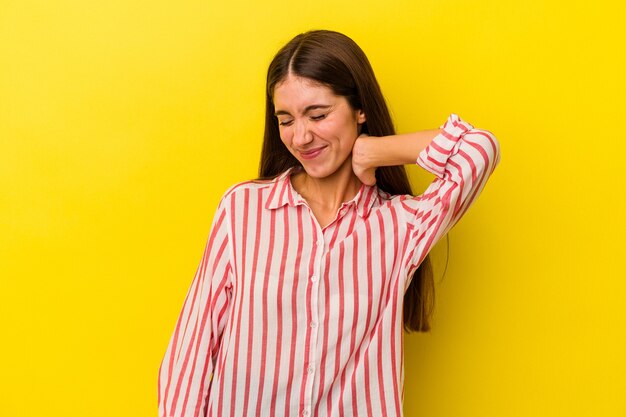 Jovem mulher caucasiana, isolada em um fundo amarelo, sofrendo de dores no pescoço devido ao estilo de vida sedentário.