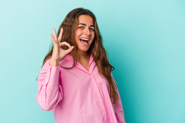 Jovem mulher caucasiana isolada em um fundo azul alegre e confiante, mostrando um gesto de ok.