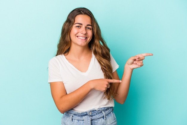 Jovem mulher caucasiana isolada em um fundo azul animada, apontando com os indicadores de distância.