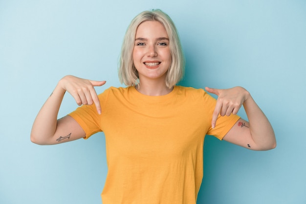 Jovem mulher caucasiana isolada em um fundo azul aponta para baixo com os dedos, sentimento positivo.