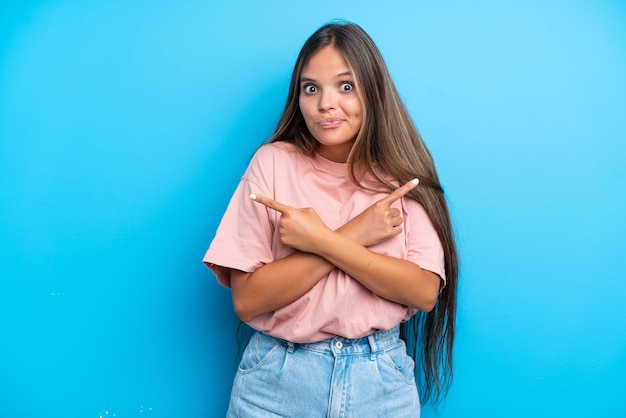 Jovem mulher caucasiana isolada em um fundo azul apontando para as laterais, tendo dúvidas