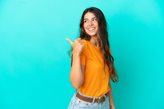 Jovem mulher caucasiana isolada em um fundo azul apontando para o lado para apresentar um produto