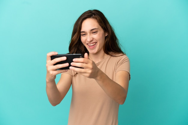 Jovem mulher caucasiana isolada em um fundo azul brincando com o celular