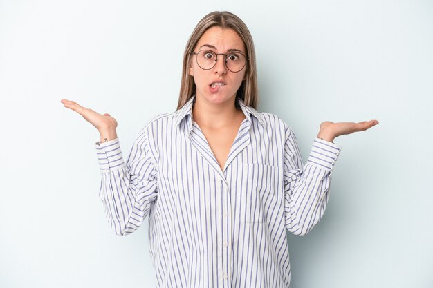 Jovem mulher caucasiana isolada em um fundo azul confusa e duvidosa, encolhendo os ombros para segurar um espaço de cópia.