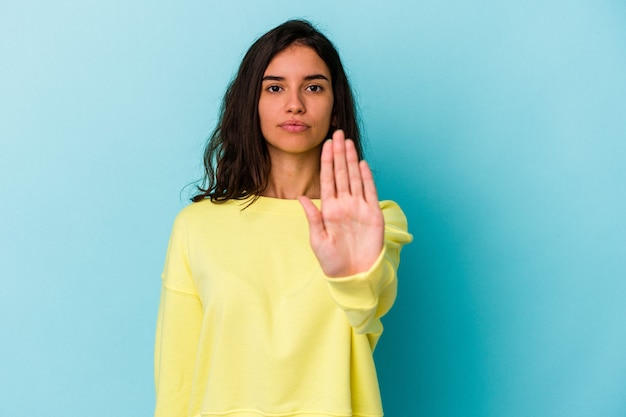 Jovem mulher caucasiana isolada em um fundo azul em pé com a mão estendida, mostrando o sinal de stop, impedindo você.