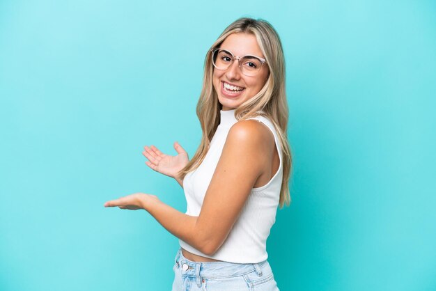 Jovem mulher caucasiana isolada em um fundo azul, estendendo as mãos para o lado para convidar para vir