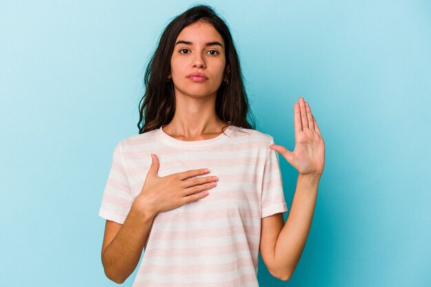 Jovem mulher caucasiana isolada em um fundo azul, fazendo um juramento, colocando a mão no peito.