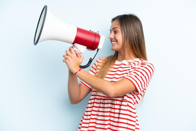 Jovem mulher caucasiana isolada em um fundo azul gritando em um megafone para anunciar algo