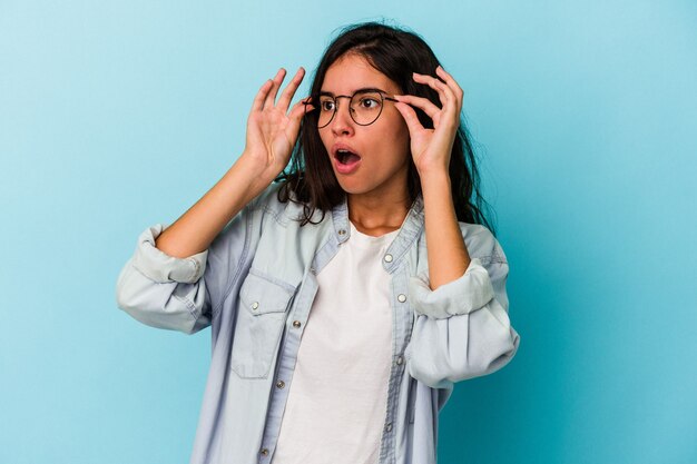 Jovem mulher caucasiana isolada em um fundo azul, mantendo os olhos abertos para encontrar uma oportunidade de sucesso.