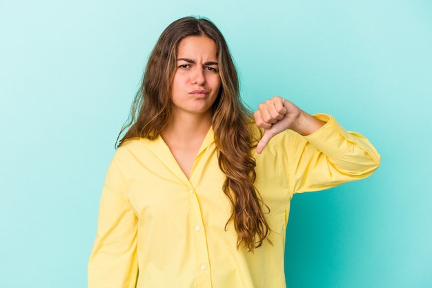 Jovem mulher caucasiana isolada em um fundo azul, mostrando o polegar para baixo, o conceito de decepção.