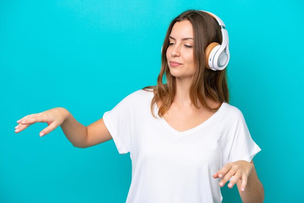 Jovem mulher caucasiana isolada em um fundo azul ouvindo música e dançando