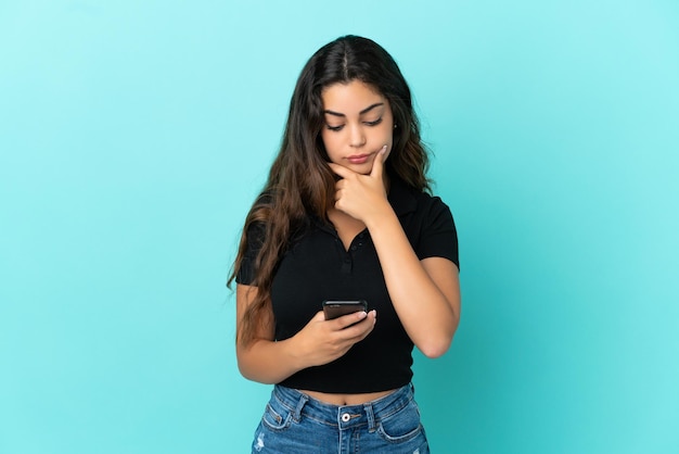 Jovem mulher caucasiana isolada em um fundo azul pensando e enviando uma mensagem