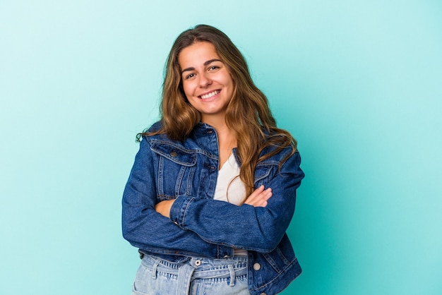 Jovem mulher caucasiana isolada em um fundo azul que se sente confiante, cruzando os braços com determinação.