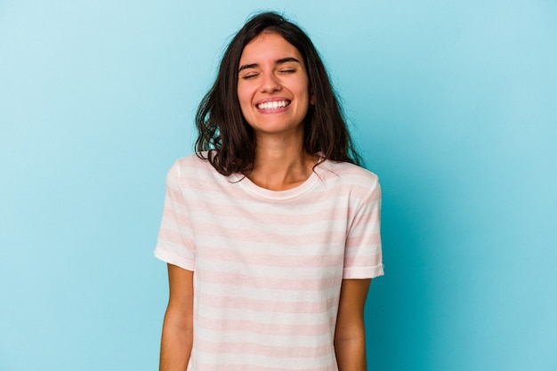 Jovem mulher caucasiana, isolada em um fundo azul, ri e fecha os olhos, sente-se relaxada e feliz.