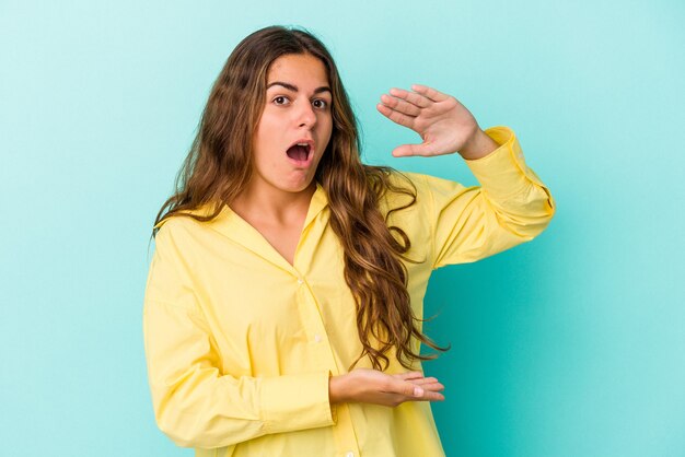 Foto jovem mulher caucasiana isolada em um fundo azul, segurando algo com as duas mãos, apresentação do produto.