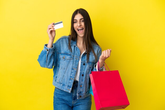 Jovem mulher caucasiana isolada em um fundo azul segurando sacolas de compras e um cartão de crédito