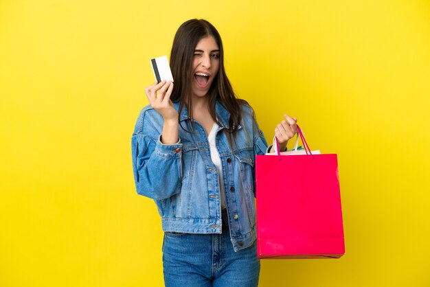 Jovem mulher caucasiana isolada em um fundo azul segurando sacolas de compras e um cartão de crédito
