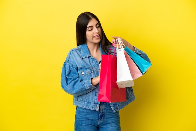 Jovem mulher caucasiana isolada em um fundo azul segurando sacolas de compras