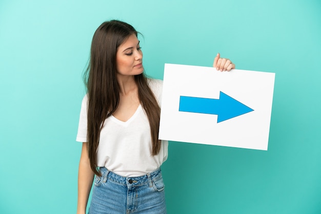 Jovem mulher caucasiana isolada em um fundo azul segurando um cartaz com o símbolo de seta