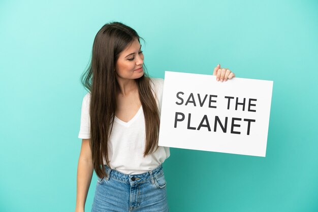 Jovem mulher caucasiana isolada em um fundo azul segurando um cartaz com o texto Salve o Planeta
