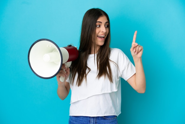 Jovem mulher caucasiana isolada em um fundo azul segurando um megafone e pretendendo descobrir a solução