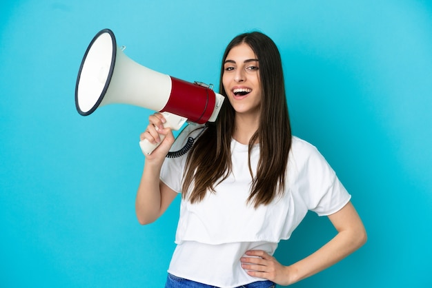 Jovem mulher caucasiana isolada em um fundo azul segurando um megafone e sorrindo