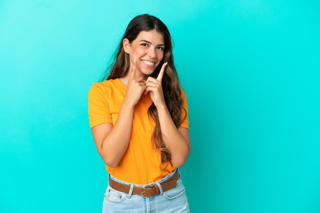 Jovem mulher caucasiana isolada em um fundo azul sorrindo com uma expressão feliz e agradável