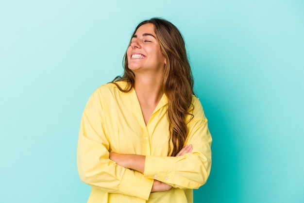 Jovem mulher caucasiana isolada em um fundo azul, sorrindo confiante com os braços cruzados.