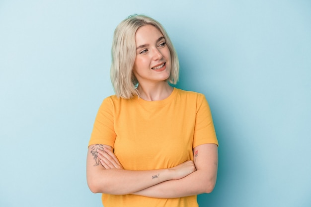 Jovem mulher caucasiana isolada em um fundo azul, sorrindo confiante com os braços cruzados.