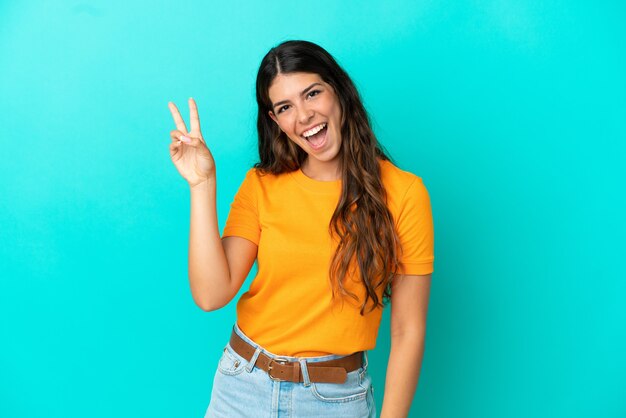 Jovem mulher caucasiana isolada em um fundo azul sorrindo e mostrando sinal de vitória