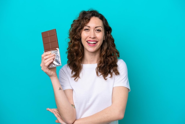 Jovem mulher caucasiana isolada em um fundo azul tomando uma pastilha de chocolate e feliz